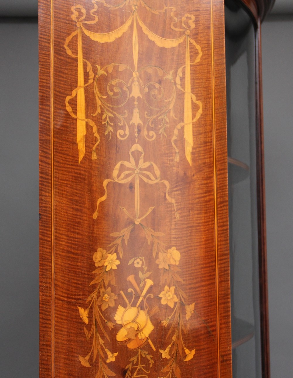 A late 19th-century bow-fronted mahogany display cabinet featuring glazed doors, satinwood marquetry inlay, slender square legs, and an undertier. View VIII