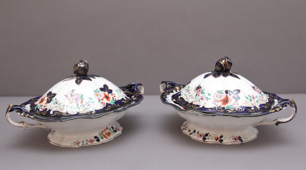 A pair of 19th-century white and cobalt blue ironstone tureens featuring hand-painted floral decoration, gilt accents, moulded handles, and flower bud finials.