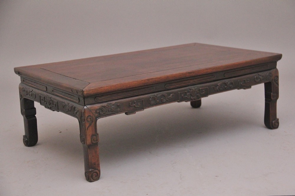 A 19th-century Chinese carved dark wood low table with a floating panel top and stylized scroll feet.