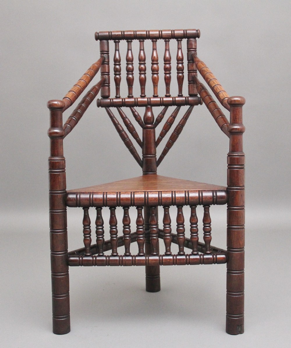 A 19th-century dark oak turners chair featuring a triangular seat, intricate bobbin-turned backrest, and sturdy turned wooden legs.