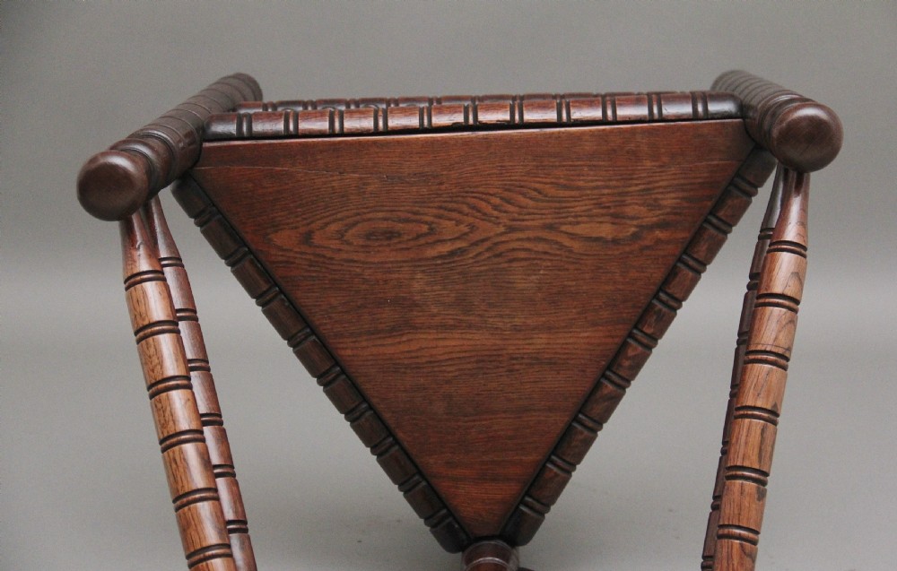 A 19th-century dark oak turners chair featuring a triangular seat, intricate bobbin-turned backrest, and sturdy turned wooden legs. View VII