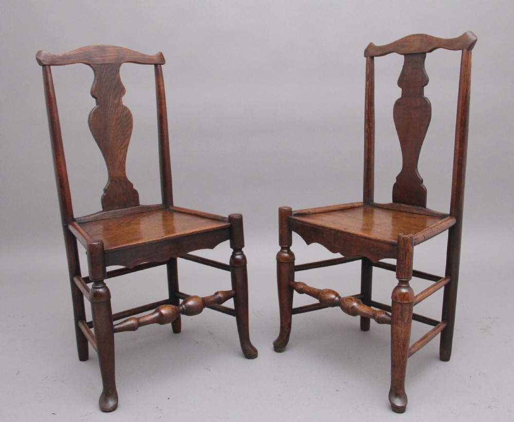 A pair of 18th-century elm side chairs featuring shaped top rails, vasiform back splats, solid wooden seats, and turned front legs with stretchers.