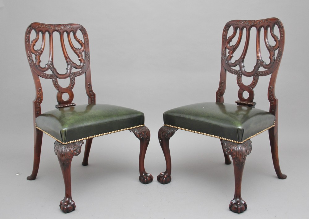 A pair of 19th-century mahogany side chairs featuring pierced carved splats, green leather seats with brass studs, and cabriole legs with ball-and-claw feet.