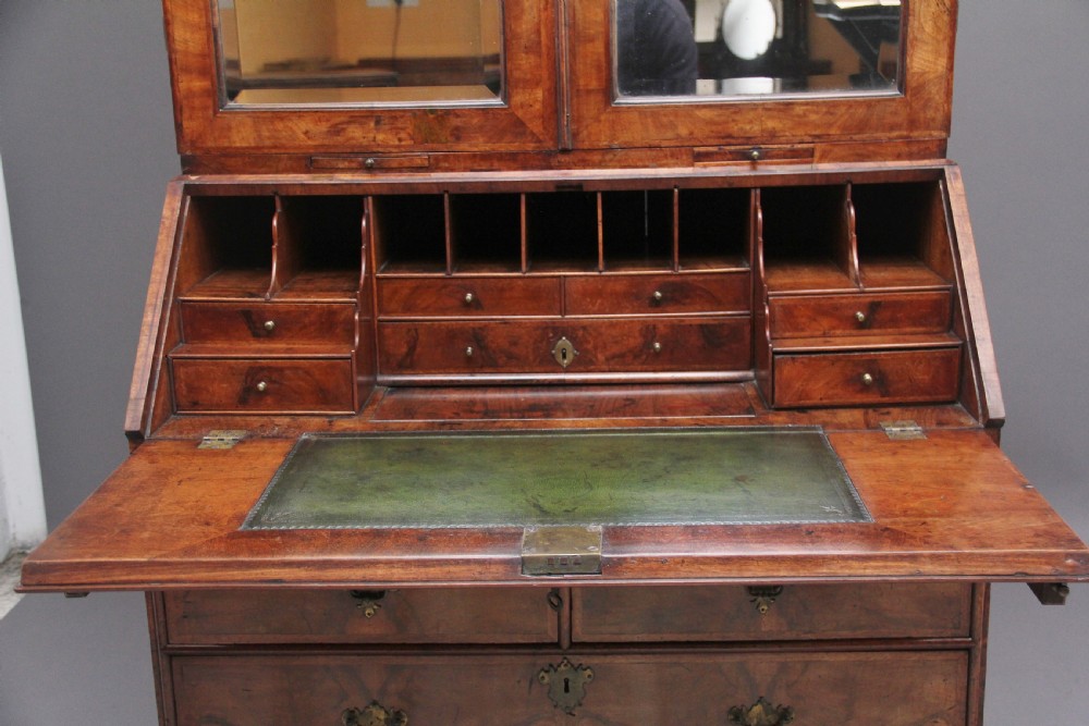 An early 18th-century walnut bureau bookcase featuring a slant-front writing desk base over drawers and an upper cabinet with two mirrored doors. View VII
