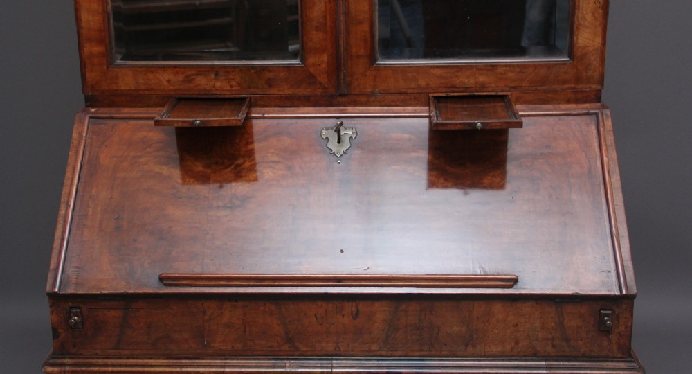 An early 18th-century walnut bureau bookcase featuring a slant-front writing desk base over drawers and an upper cabinet with two mirrored doors. View IX