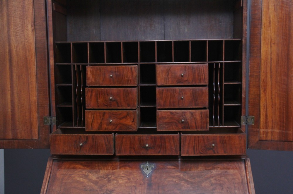 An early 18th-century walnut bureau bookcase featuring a slant-front writing desk base over drawers and an upper cabinet with two mirrored doors. View X
