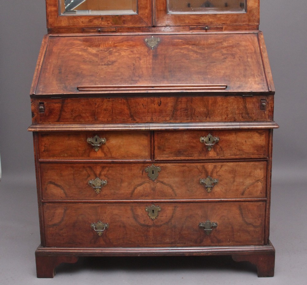 An early 18th-century walnut bureau bookcase featuring a slant-front writing desk base over drawers and an upper cabinet with two mirrored doors. View XI