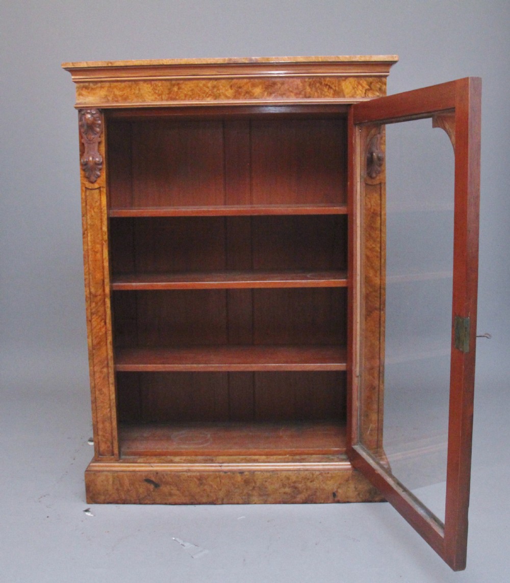 A Victorian burr walnut glazed cabinet featuring an arched glass door, carved corbels, three internal shelves, and a solid plinth base. View II