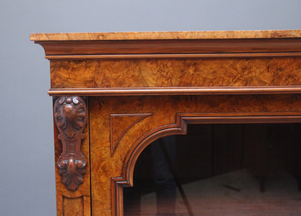 A Victorian burr walnut glazed cabinet featuring an arched glass door, carved corbels, three internal shelves, and a solid plinth base. View III