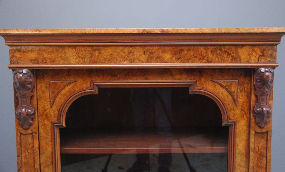 A Victorian burr walnut glazed cabinet featuring an arched glass door, carved corbels, three internal shelves, and a solid plinth base. View IV