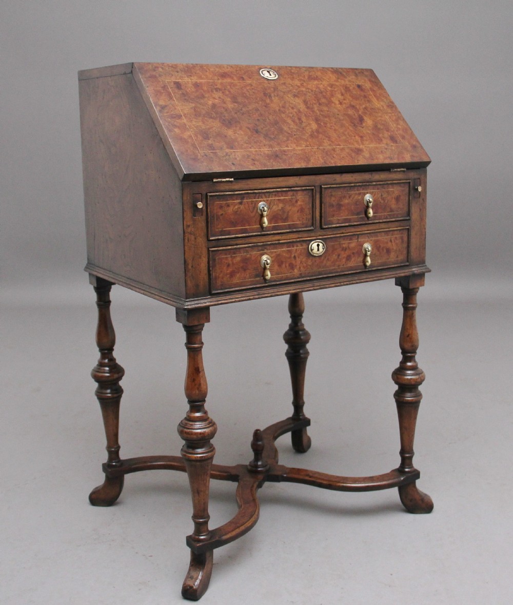 An early 20th-century walnut writing bureau on stand with a sloped fall front, lower drawers, and turned legs with a shaped cross-stretcher.