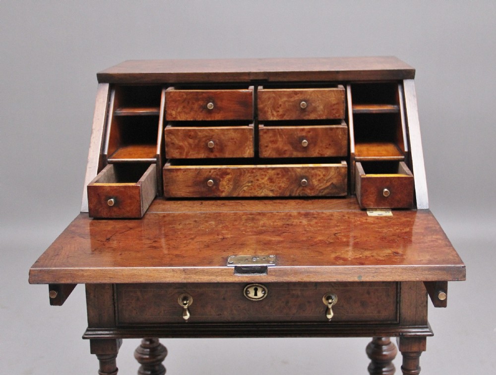 An early 20th-century walnut writing bureau on stand with a sloped fall front, lower drawers, and turned legs with a shaped cross-stretcher. View VI