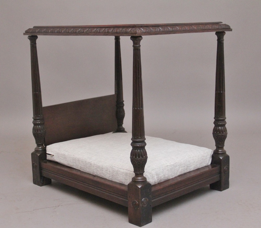 A nineteenth-century mahogany four-poster dog bed featuring carved reeded posts, a moulded canopy frame, and a neutral fabric cushion.