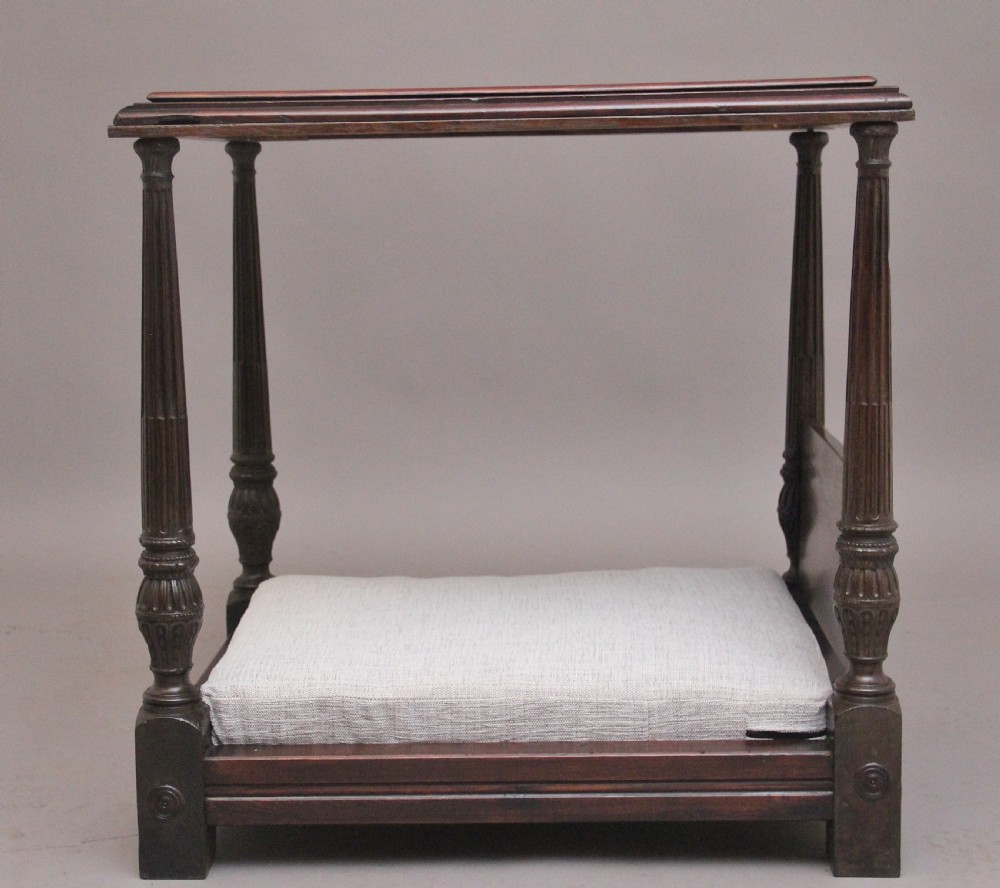 A nineteenth-century mahogany four-poster dog bed featuring carved reeded posts, a moulded canopy frame, and a neutral fabric cushion. View V