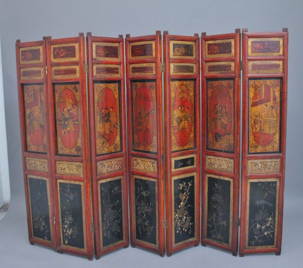 An early 20th-century seven-panel Chinese folding screen featuring crimson and black lacquered sections decorated with hand-painted figures and gilded floral borders.