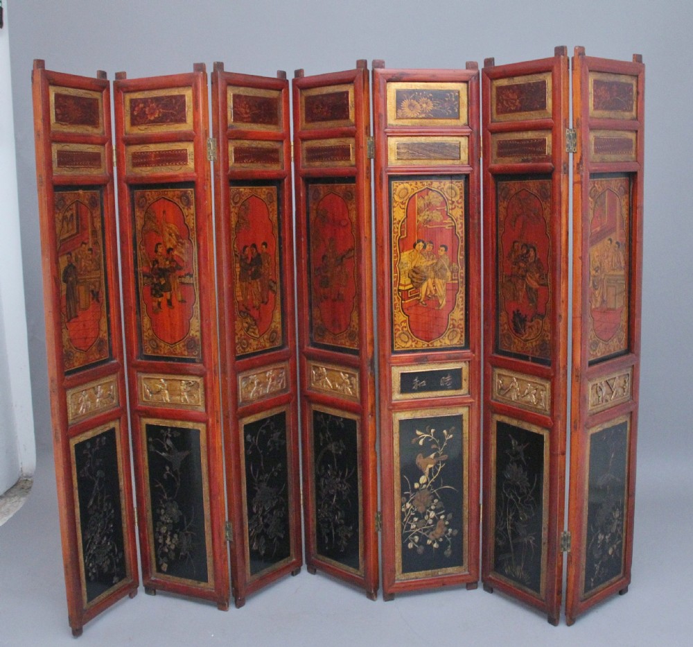 An early 20th-century seven-panel Chinese folding screen featuring crimson and black lacquered sections decorated with hand-painted figures and gilded floral borders. View IV