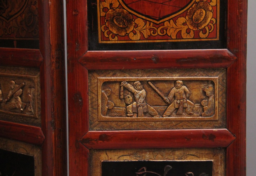 An early 20th-century seven-panel Chinese folding screen featuring crimson and black lacquered sections decorated with hand-painted figures and gilded floral borders. View X