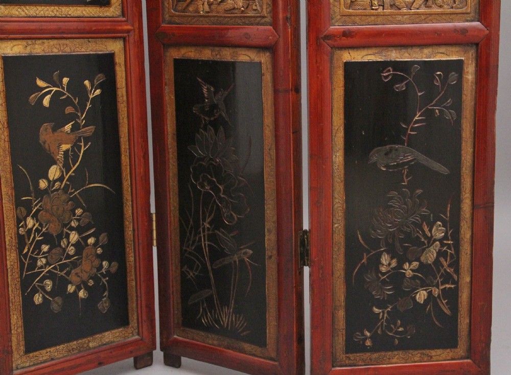 An early 20th-century seven-panel Chinese folding screen featuring crimson and black lacquered sections decorated with hand-painted figures and gilded floral borders. View XIII
