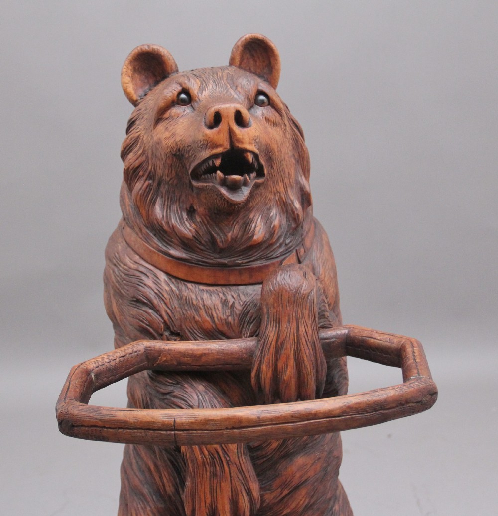 A 19th-century carved wooden Black Forest stick stand featuring a full-length standing bear holding an oval ring above a carved base with a metal drip tray. View VI