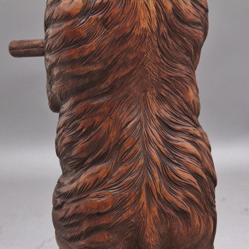 A 19th-century carved wooden Black Forest stick stand featuring a full-length standing bear holding an oval ring above a carved base with a metal drip tray. View X