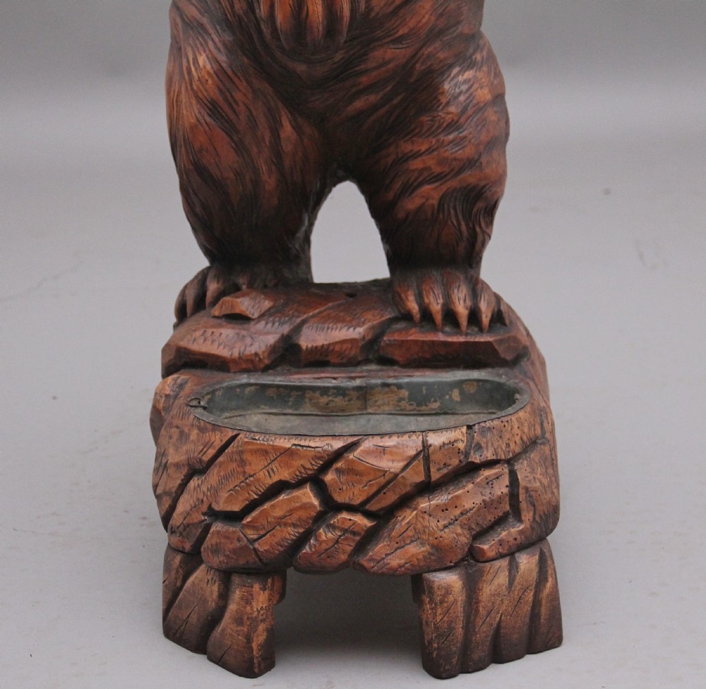 A 19th-century carved wooden Black Forest stick stand featuring a full-length standing bear holding an oval ring above a carved base with a metal drip tray. View XI