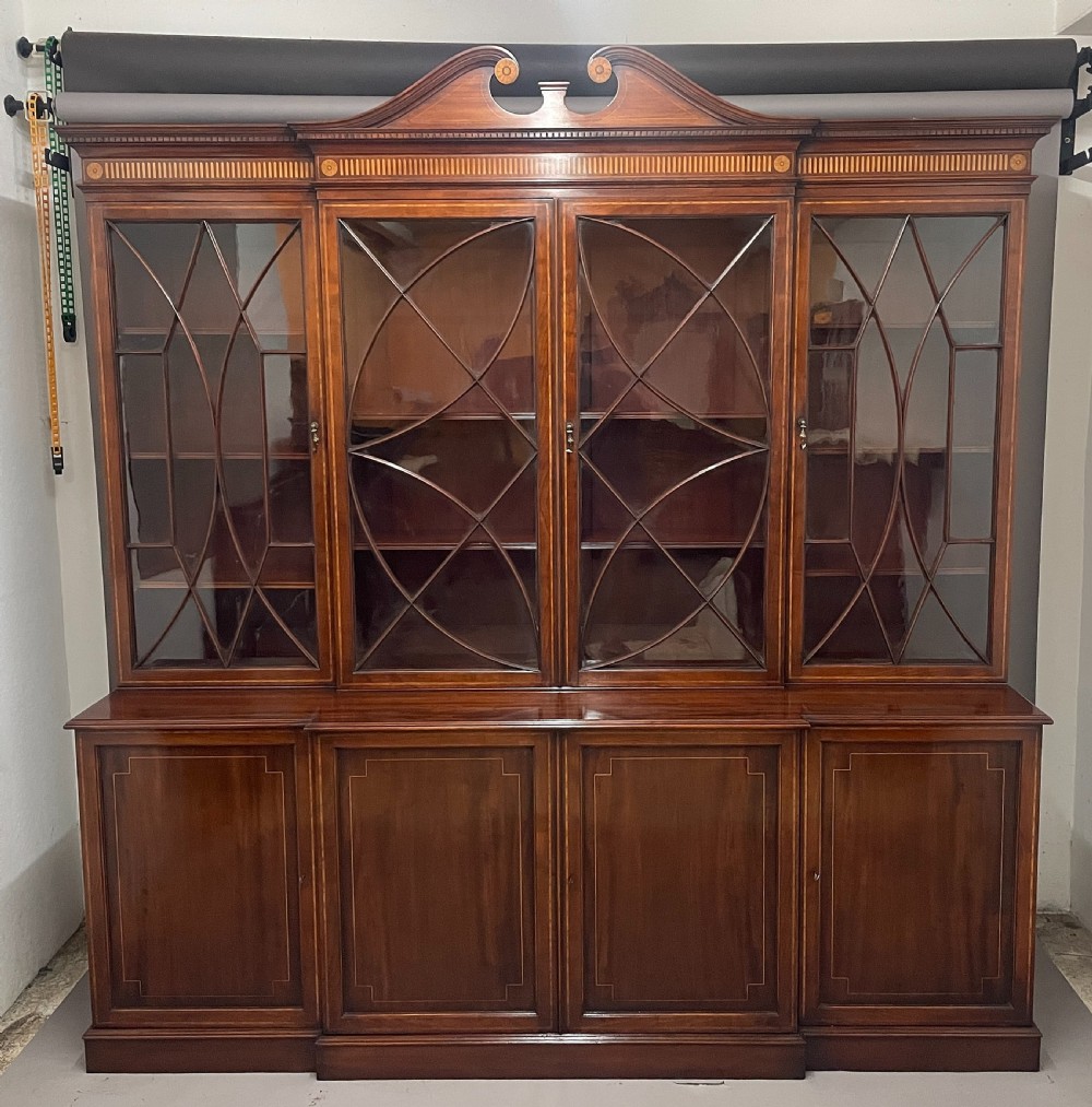 A 19th-century mahogany breakfront bookcase featuring a swan-neck pediment, geometrically glazed upper doors, and inlaid lower cupboard doors.