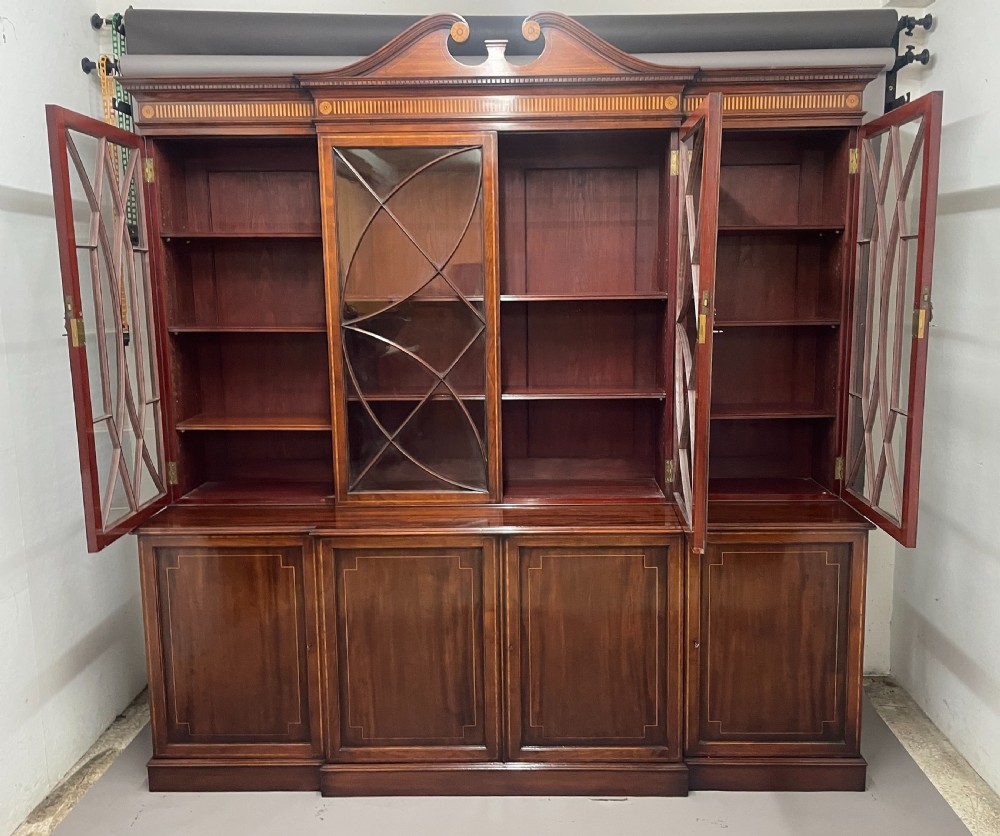 A 19th-century mahogany breakfront bookcase featuring a swan-neck pediment, geometrically glazed upper doors, and inlaid lower cupboard doors. View II