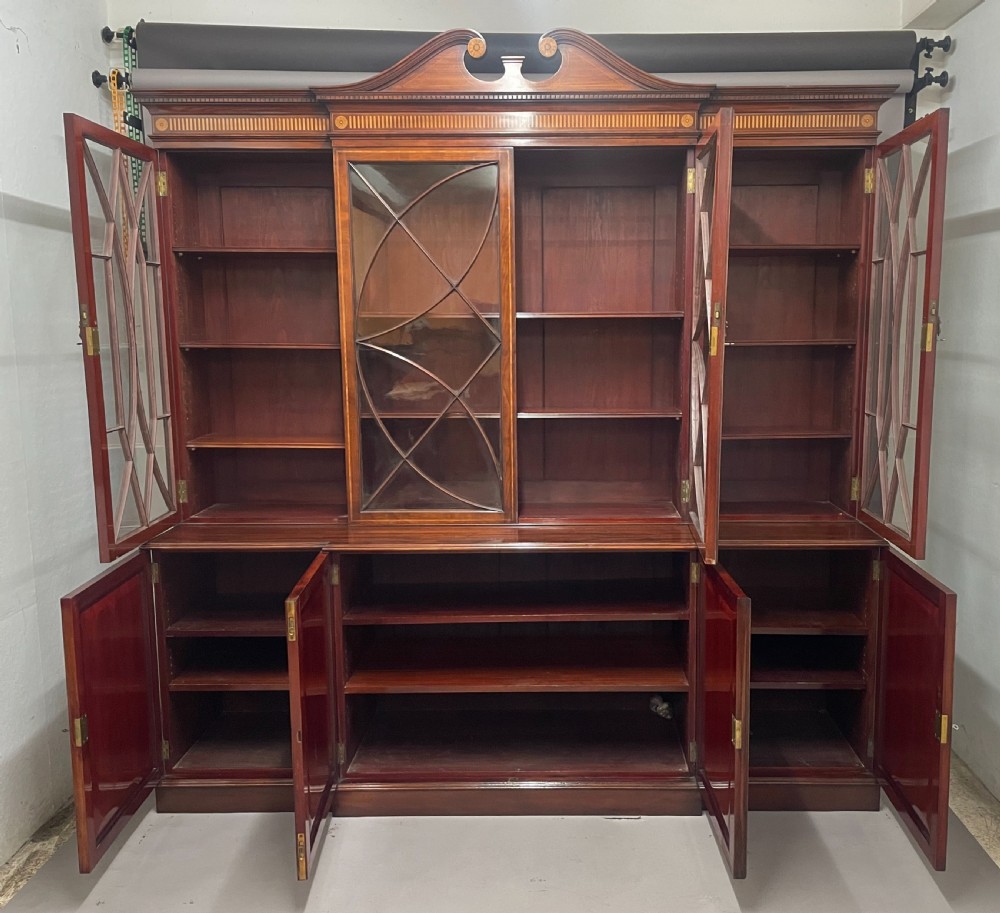 A 19th-century mahogany breakfront bookcase featuring a swan-neck pediment, geometrically glazed upper doors, and inlaid lower cupboard doors. View III