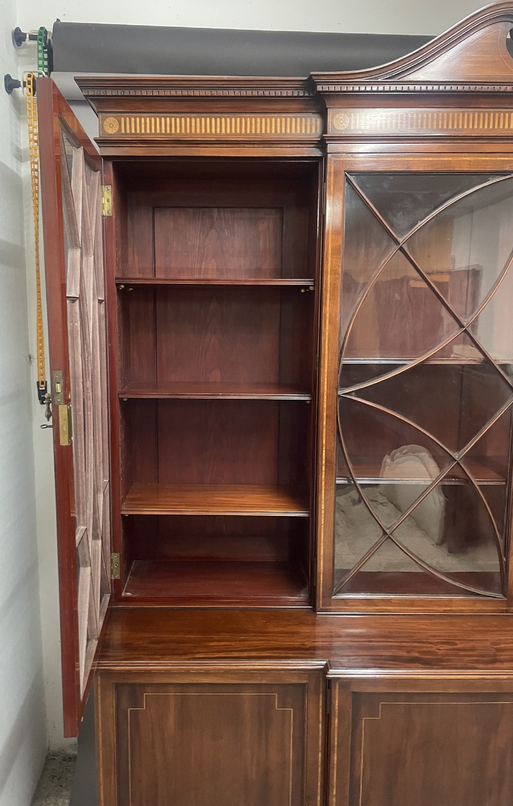 A 19th-century mahogany breakfront bookcase featuring a swan-neck pediment, geometrically glazed upper doors, and inlaid lower cupboard doors. View IV