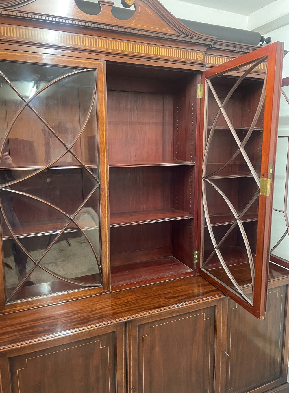 A 19th-century mahogany breakfront bookcase featuring a swan-neck pediment, geometrically glazed upper doors, and inlaid lower cupboard doors. View V