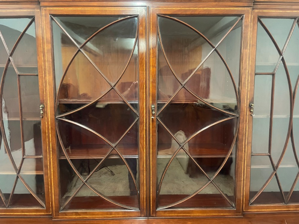 A 19th-century mahogany breakfront bookcase featuring a swan-neck pediment, geometrically glazed upper doors, and inlaid lower cupboard doors. View VI
