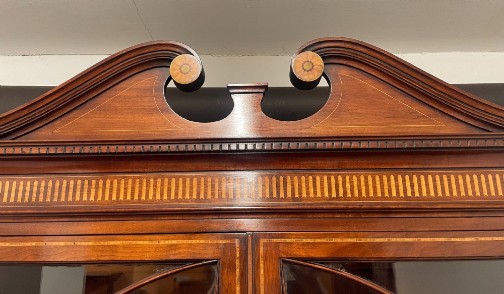 A 19th-century mahogany breakfront bookcase featuring a swan-neck pediment, geometrically glazed upper doors, and inlaid lower cupboard doors. View VII