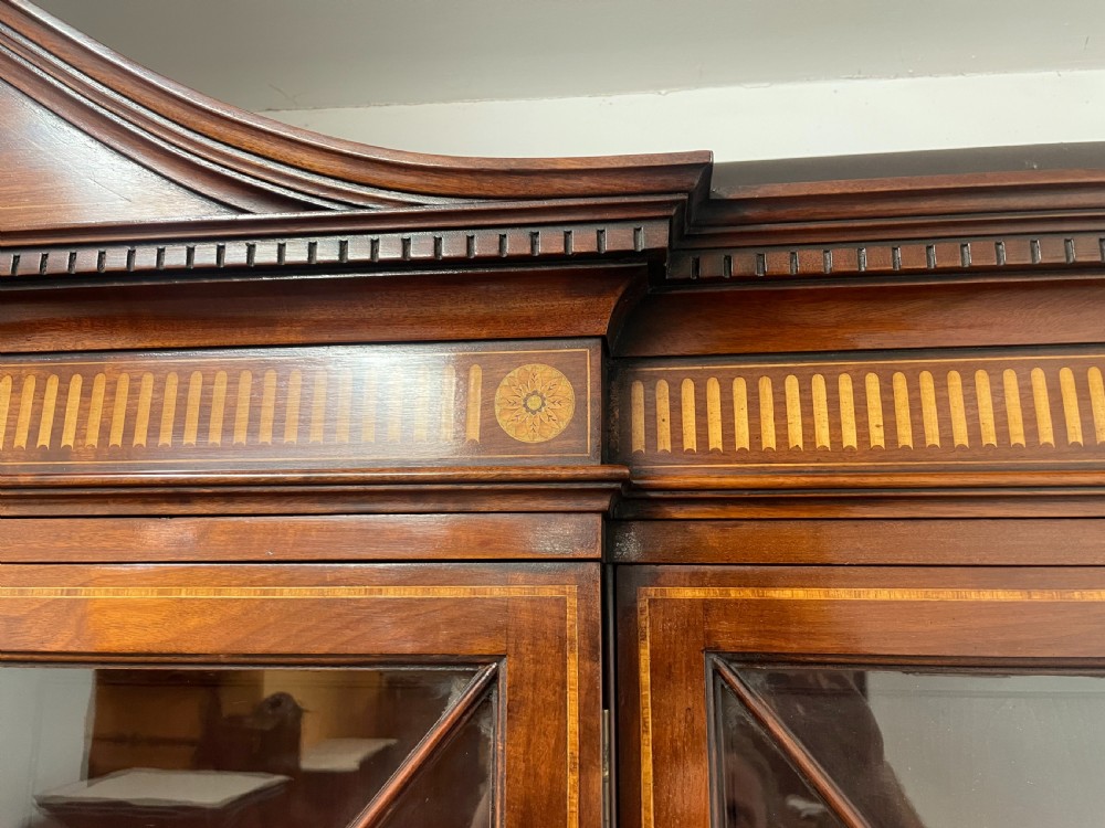 A 19th-century mahogany breakfront bookcase featuring a swan-neck pediment, geometrically glazed upper doors, and inlaid lower cupboard doors. View IX