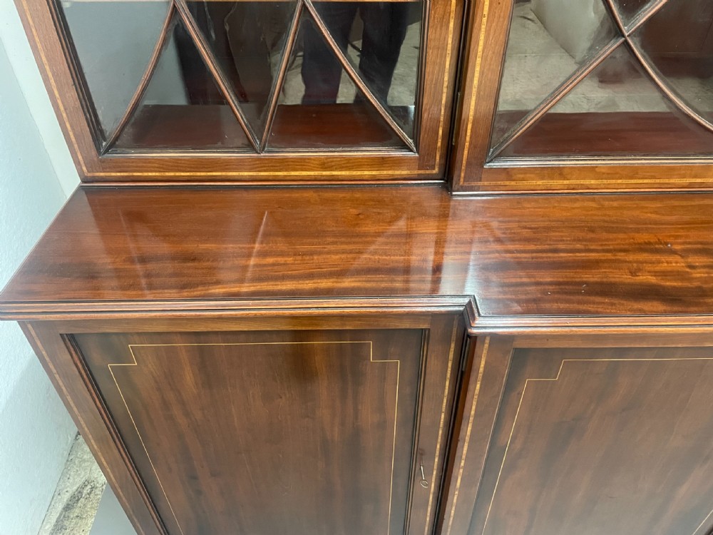 A 19th-century mahogany breakfront bookcase featuring a swan-neck pediment, geometrically glazed upper doors, and inlaid lower cupboard doors. View X