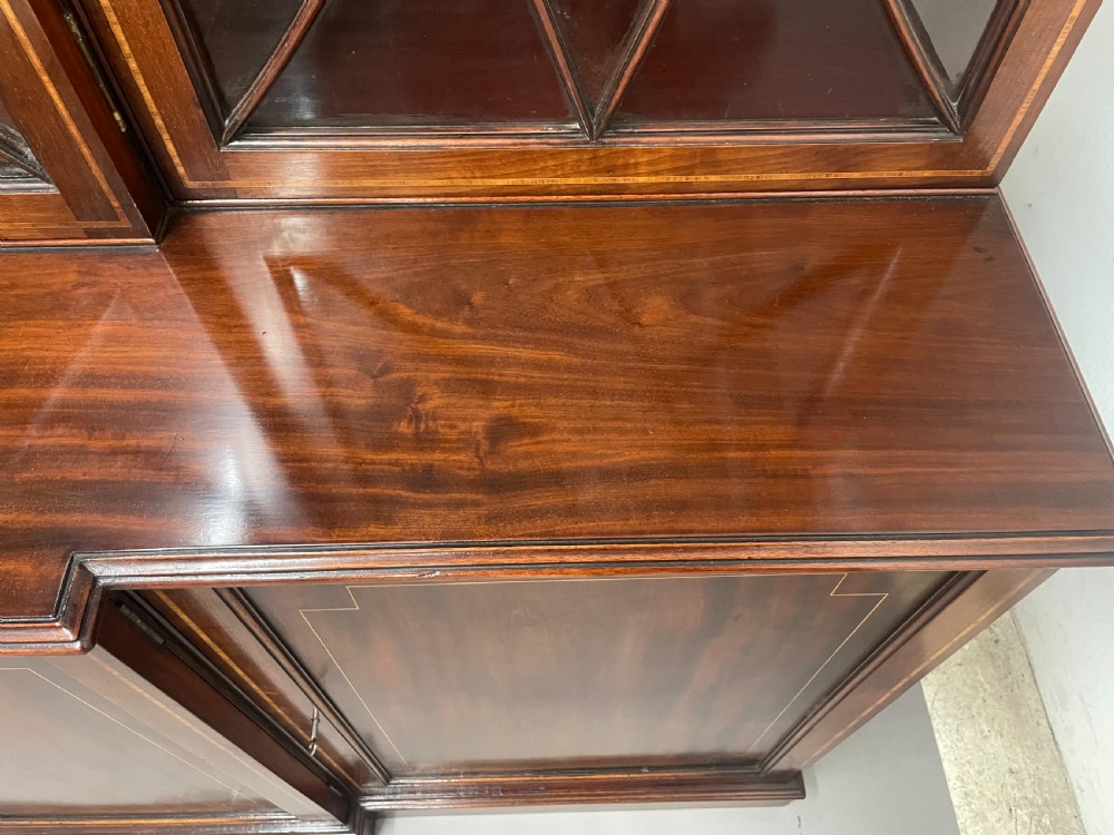 A 19th-century mahogany breakfront bookcase featuring a swan-neck pediment, geometrically glazed upper doors, and inlaid lower cupboard doors. View XI