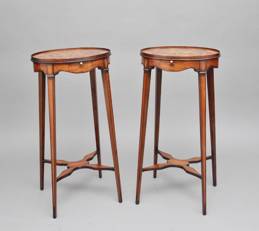 A pair of tall, oval-topped mahogany urn stands featuring central floral marquetry inlays, pull-out slides, square tapered legs, and curved X-form stretchers.
