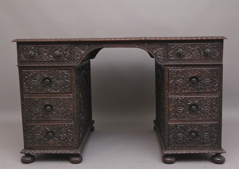 A dark wood double pedestal partners desk featuring intricate relief floral carvings across all drawers, side panels, and top borders.