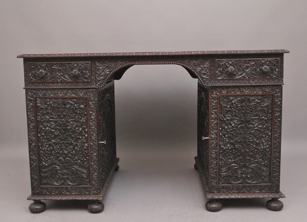 A dark wood double pedestal partners desk featuring intricate relief floral carvings across all drawers, side panels, and top borders. View IV