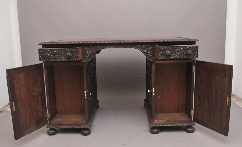 A dark wood double pedestal partners desk featuring intricate relief floral carvings across all drawers, side panels, and top borders. View V