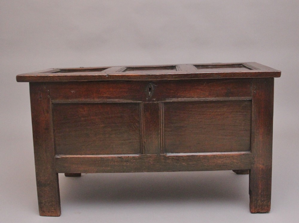 An 18th-century dark oak coffer featuring a three-panel hinged top, twin-panelled front, central keyhole escutcheon, and sturdy stile legs.