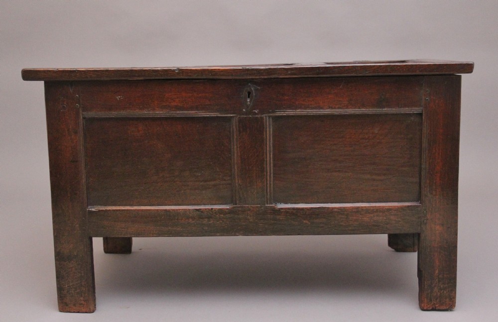 An 18th-century dark oak coffer featuring a three-panel hinged top, twin-panelled front, central keyhole escutcheon, and sturdy stile legs. View III