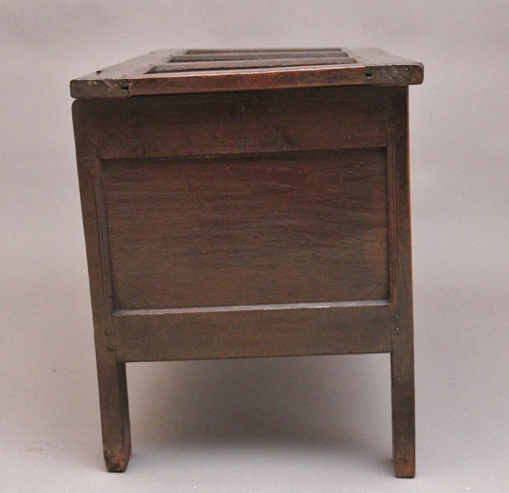 An 18th-century dark oak coffer featuring a three-panel hinged top, twin-panelled front, central keyhole escutcheon, and sturdy stile legs. View V