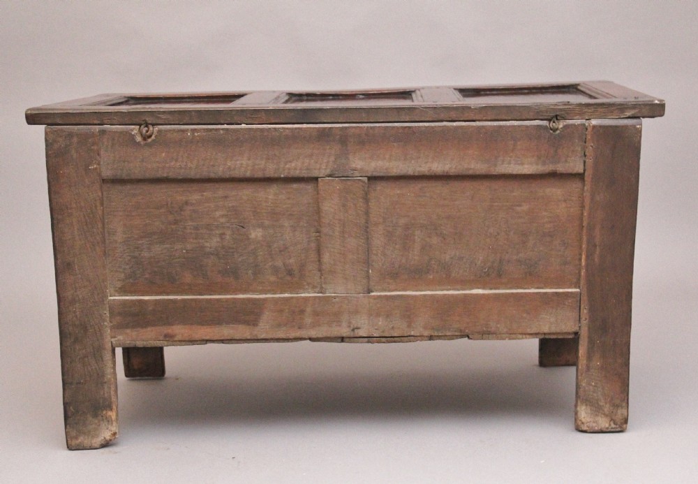An 18th-century dark oak coffer featuring a three-panel hinged top, twin-panelled front, central keyhole escutcheon, and sturdy stile legs. View VI