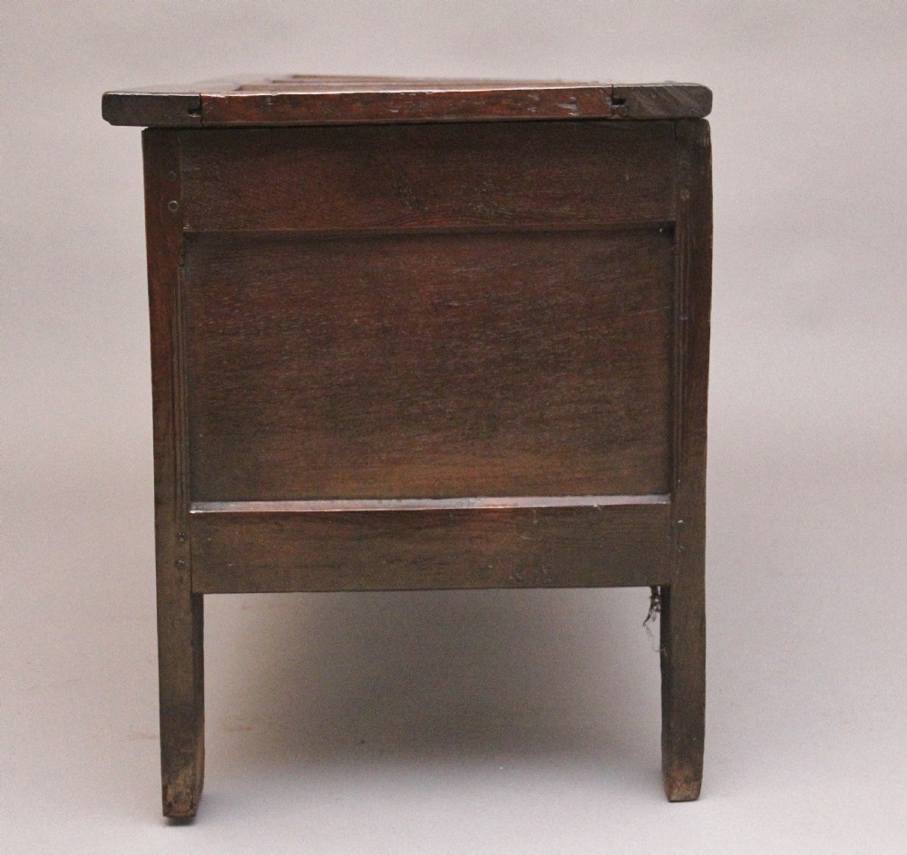 An 18th-century dark oak coffer featuring a three-panel hinged top, twin-panelled front, central keyhole escutcheon, and sturdy stile legs. View VII