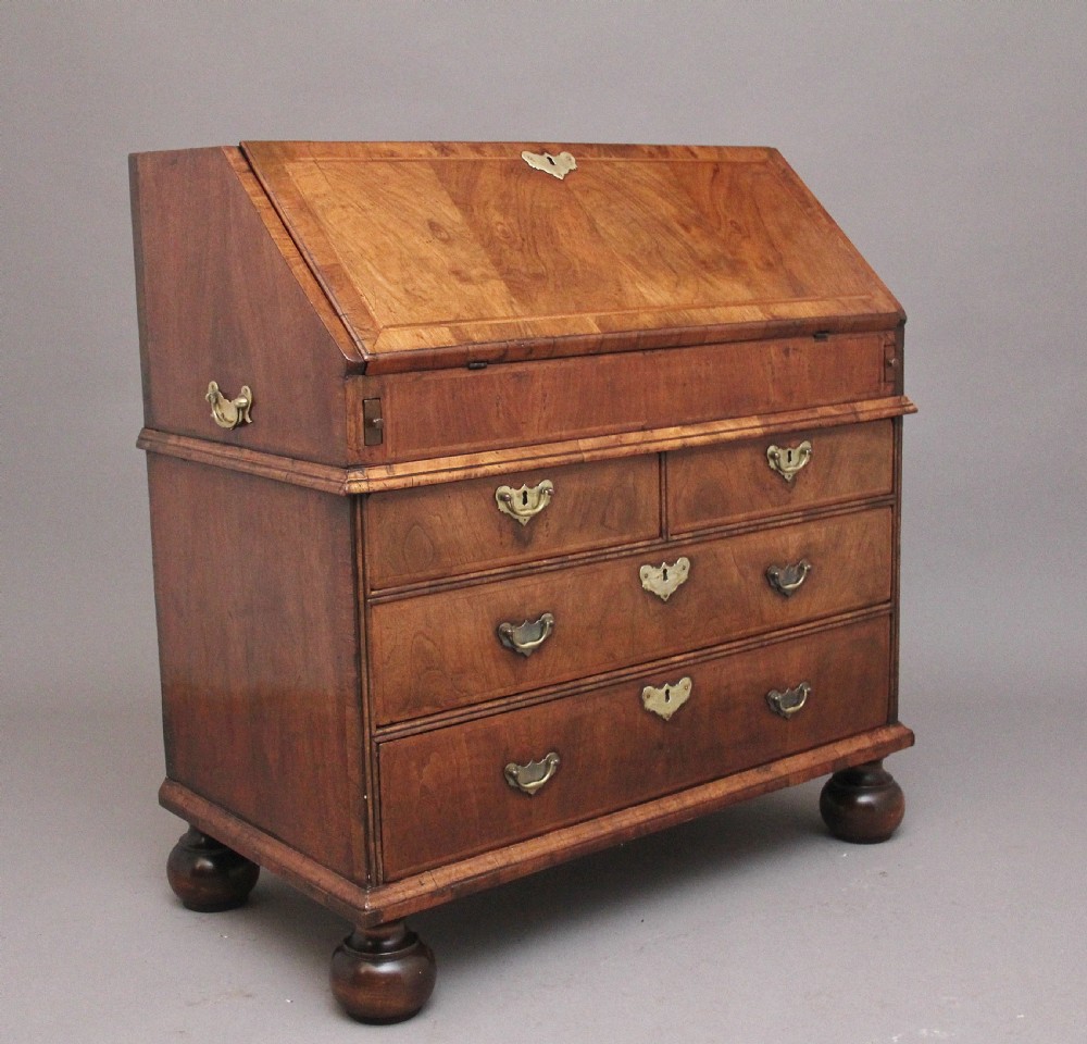 An 18th century walnut writing bureau featuring a sloped fall-front lid, brass drop handles, keyhole escutcheons, and turned ball feet.