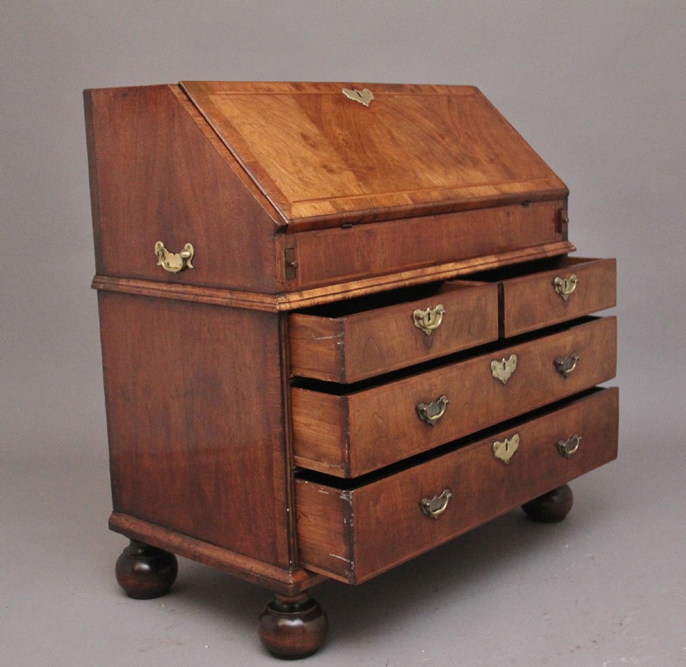An 18th century walnut writing bureau featuring a sloped fall-front lid, brass drop handles, keyhole escutcheons, and turned ball feet. View IV