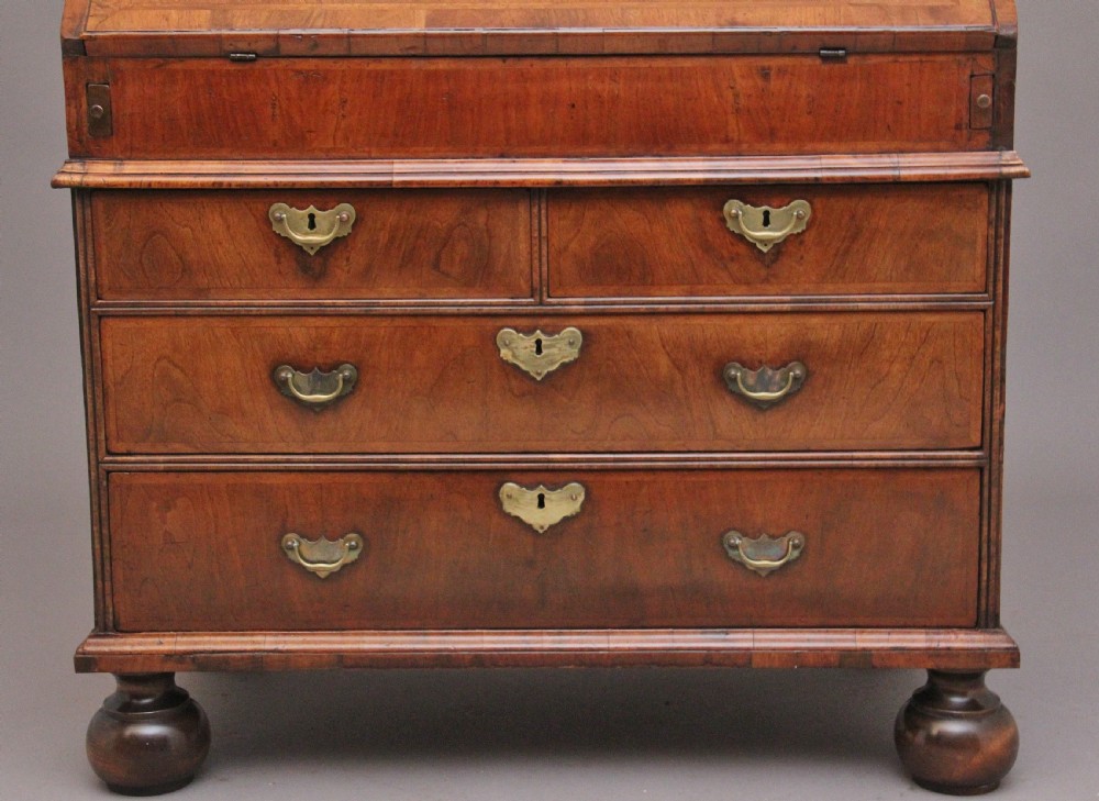 An 18th century walnut writing bureau featuring a sloped fall-front lid, brass drop handles, keyhole escutcheons, and turned ball feet. View V
