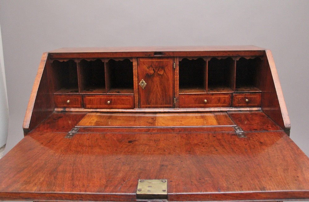 An 18th century walnut writing bureau featuring a sloped fall-front lid, brass drop handles, keyhole escutcheons, and turned ball feet. View VI