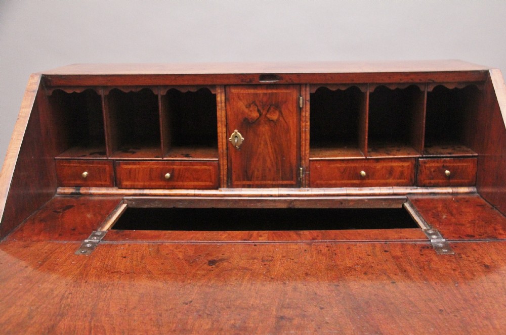 An 18th century walnut writing bureau featuring a sloped fall-front lid, brass drop handles, keyhole escutcheons, and turned ball feet. View VII