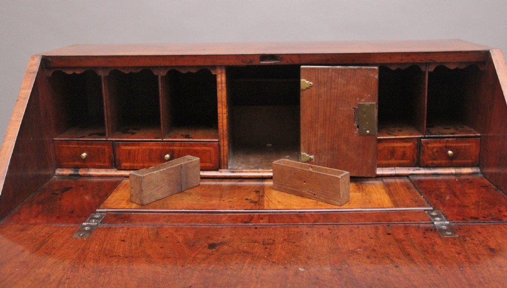 An 18th century walnut writing bureau featuring a sloped fall-front lid, brass drop handles, keyhole escutcheons, and turned ball feet. View VIII